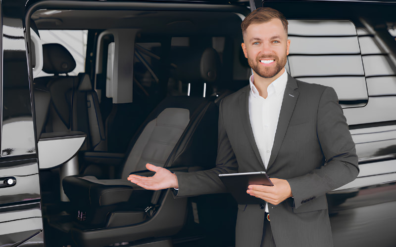 Smiling chauffeur beside a black executive passenger van