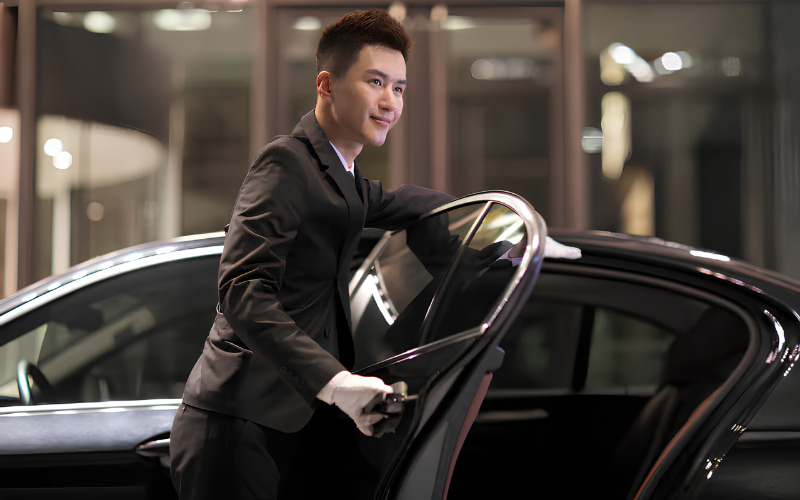 Chauffeur opening a black car door for passenger pickup